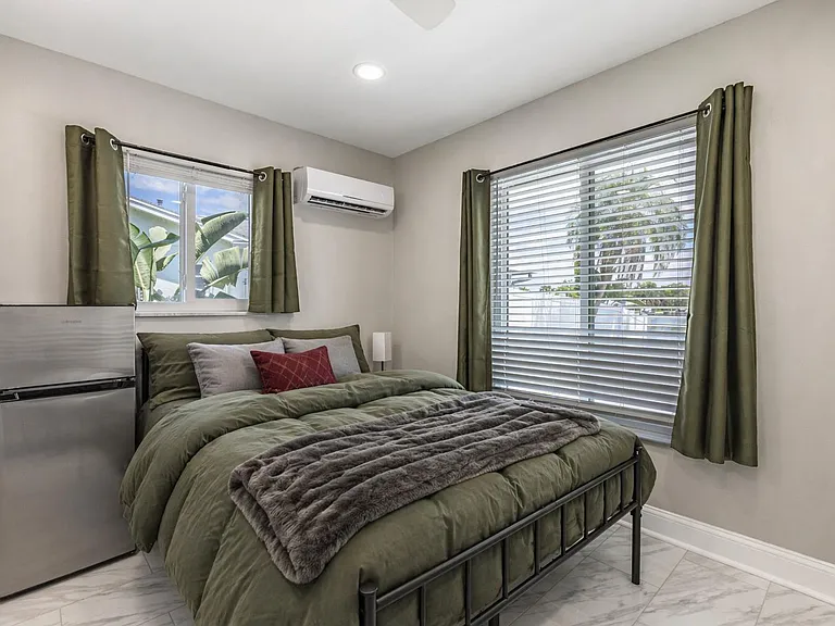 Well-appointed bedroom with a full bed, two large windows with a mini fridge and wall A/C.