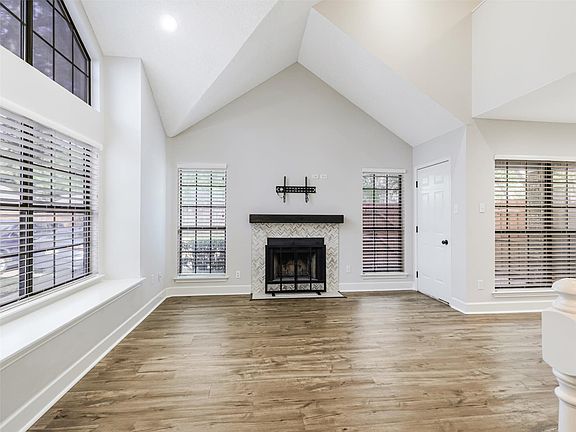 Vaulted ceilings featuring a fireplace with a chevron-pattern tile surround and a dark wood mantel, wood-finish flooring, and expansive windows with built-in window seating