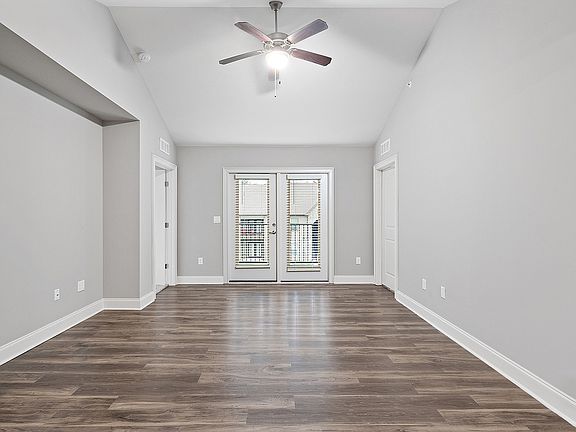 Bright and spacious living area with elegant wooden flooring, modern ceiling fan, and double doors leading to a balcony.
