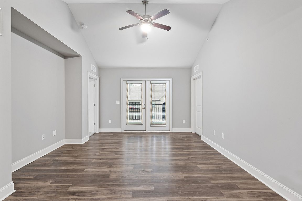 Bright and spacious living area with elegant wooden flooring, modern ceiling fan, and double doors leading to a balcony.