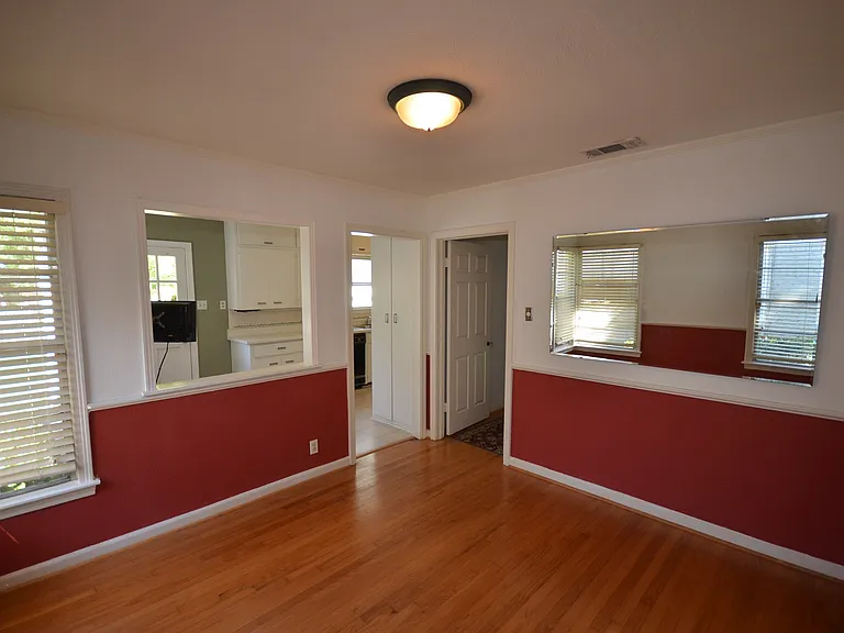 Hardwood flooring throughout, featuring a pass-through opening to the kitchen, a built-in wall mirror, and privacy blinds on windows.