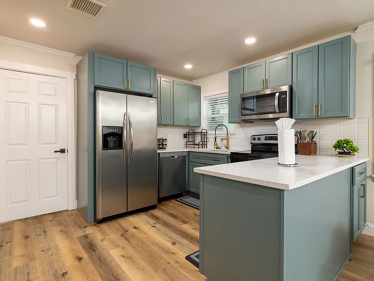 Bright, modern kitchen with stainless appliances, teal cabinets, and a spacious island_perfect for cooking, gathering, and enjoying a warm, stylish space.