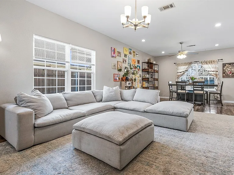 Spacious living area featuring light-toned walls, wood-finish flooring, and a dining space with a ceiling fan