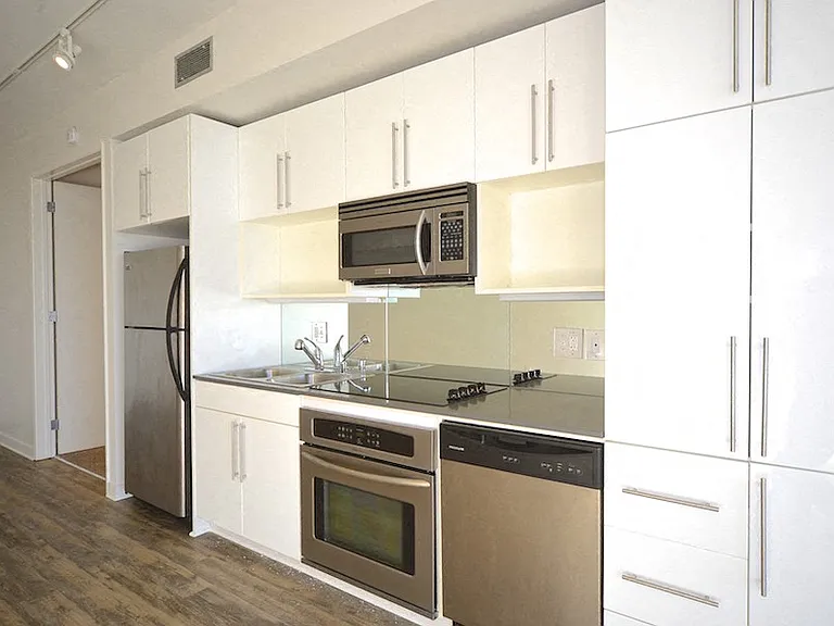 Kitchen area with spacious white cabinets, electronic stove/oven, microwave, dishwasher, and refridgerator at 12th Street Lofts in National City, California.