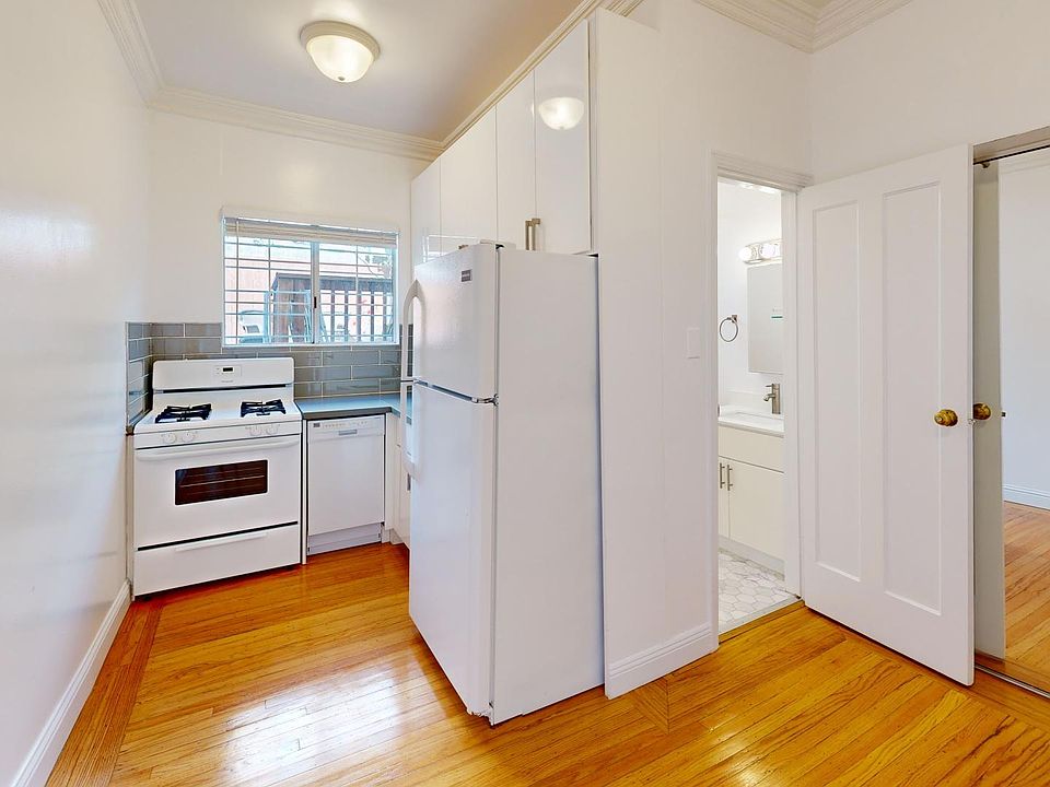 Kitchen with stove, refrigerator, closet with mirror, wood-like flooring, and an entrance to the bathroom