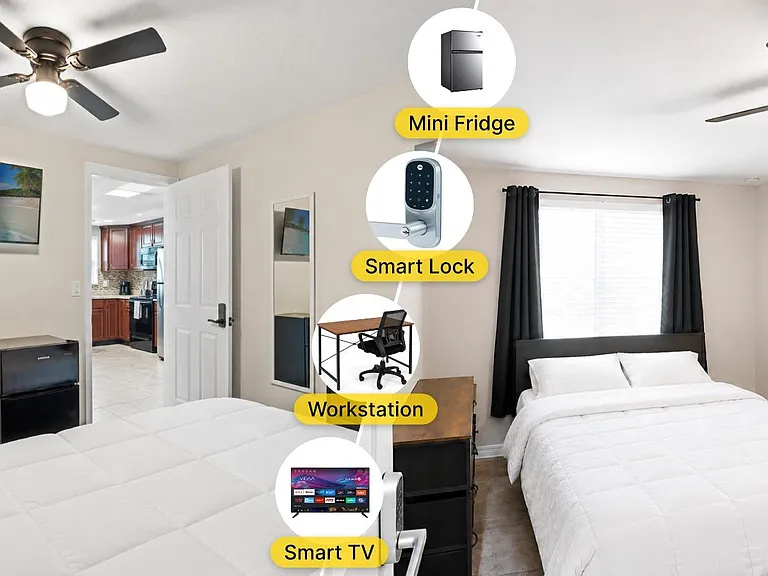 Furnished bedroom with two beds, a mini fridge, desk setup, smart TV, ceiling fan, and a large window with curtains.
