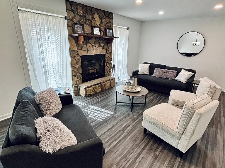 Living room with seating area, stone fireplace, recessed lighting, and large windows with curtains for natural light.