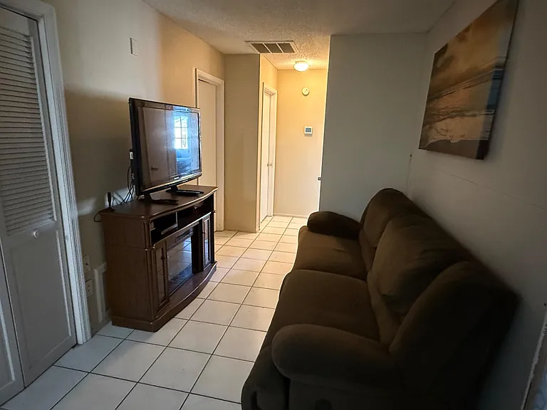 Compact lounge area with tile flooring, comfortable seating, and a TV setupideal for relaxing between rooms.