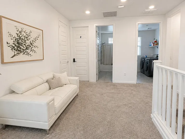 Upstairs loft with plush carpeting, recessed lighting, and a comfortable seating area near the laundry and bath.