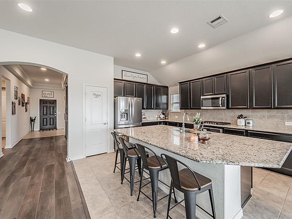 Expansive kitchen island with a granite countertop, dark cabinetry, and stainless steel appliances