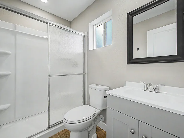 Clean full bath with tub/shower combo, sliding glass enclosure, vanity storage, and a frosted window for privacy.