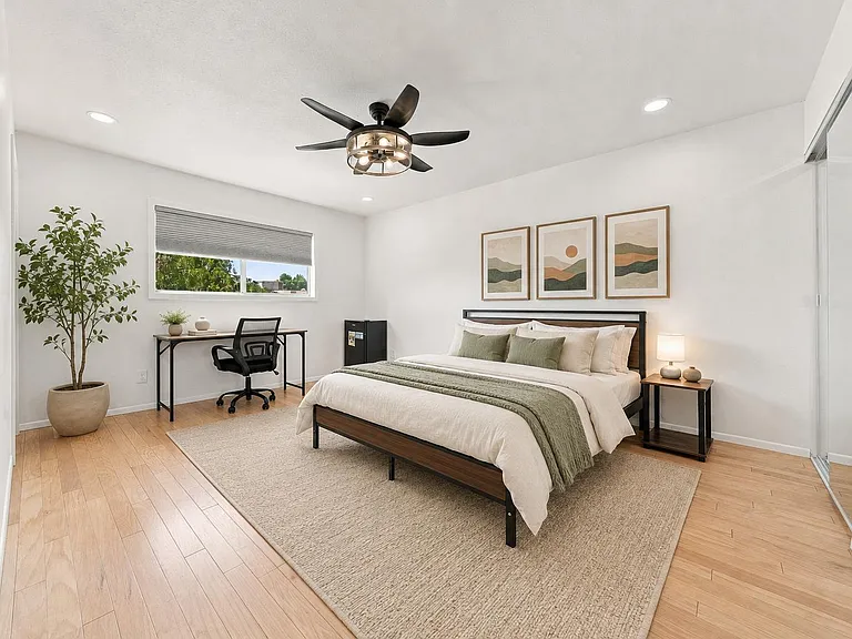 Spacious bedroom with a full bed, work desk, ceiling fan, and mirrored closet doors plus a large window for daylight.
