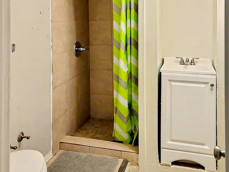 Compact bathroom with a tiled walk-in shower, curtain rod, and a vanity sink for everyday convenience.