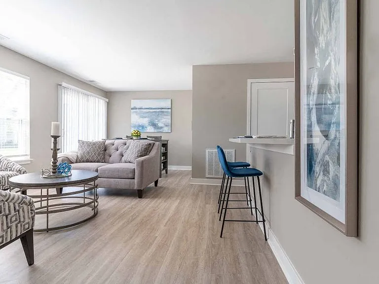 View of great room from the foyer showing living area seating, kitchen breakfast bar, large windows, dining room table ar the far end and sliding glass doors to the private patio or balcony