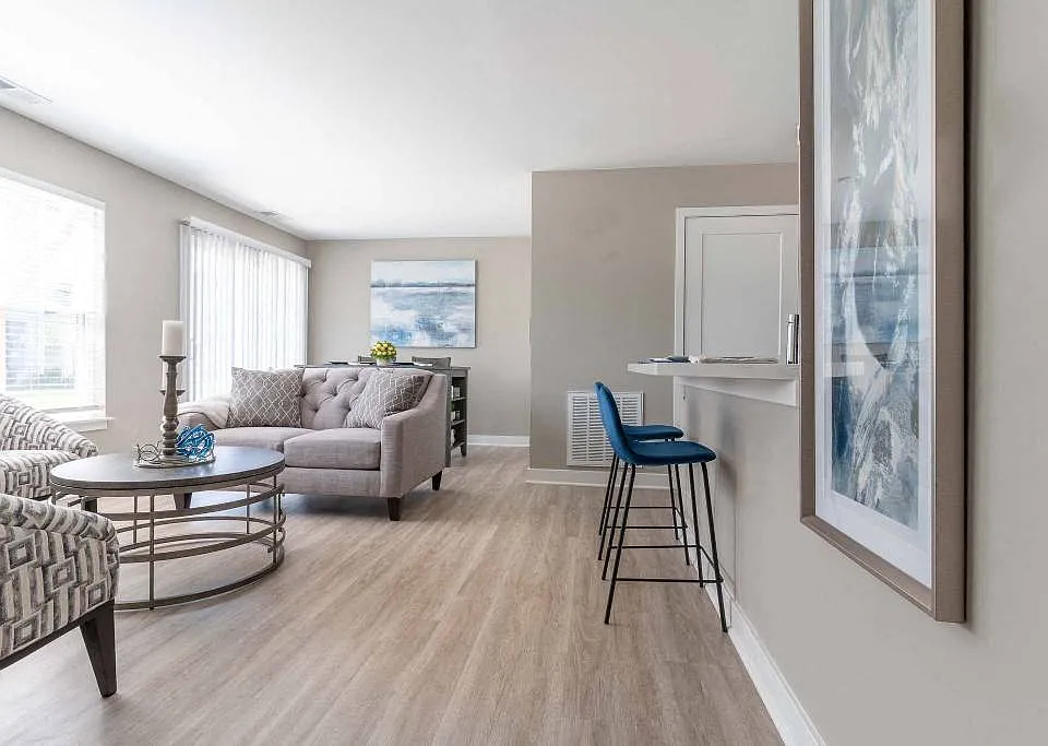 View of great room from the foyer showing living area seating, kitchen breakfast bar, large windows, dining room table ar the far end and sliding glass doors to the private patio or balcony