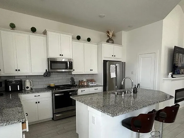 Open kitchen with granite island seating, ample white cabinetry, and stainless-steel appliances for everyday cooking.