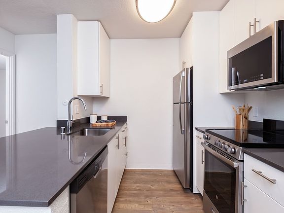Kitchen with white cabinetry, dark grey countertops, stainless steel appliances and hard surface flooring