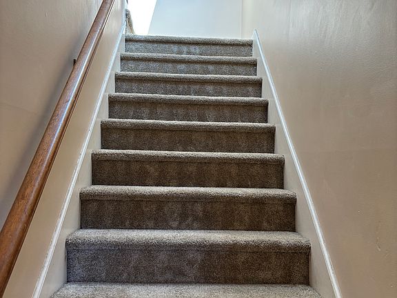 Tiled entrance with coat hooks on left leading to carpeted stairs to living room.