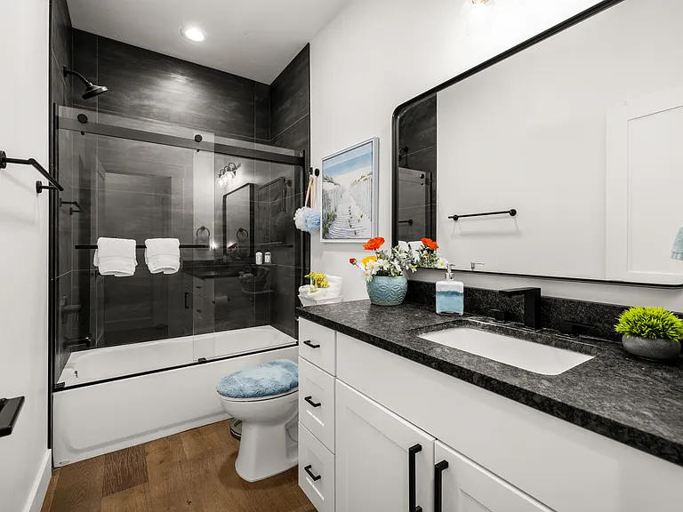 Elegant en-suite bath featuring sleek black finishes, granite countertops, and a glass-enclosed shower, creating a refined and welcoming retreat for the suite.