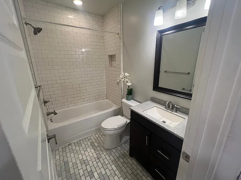Fully renovated bathroom with tiled floors and shower. Modern vanity and lighting.