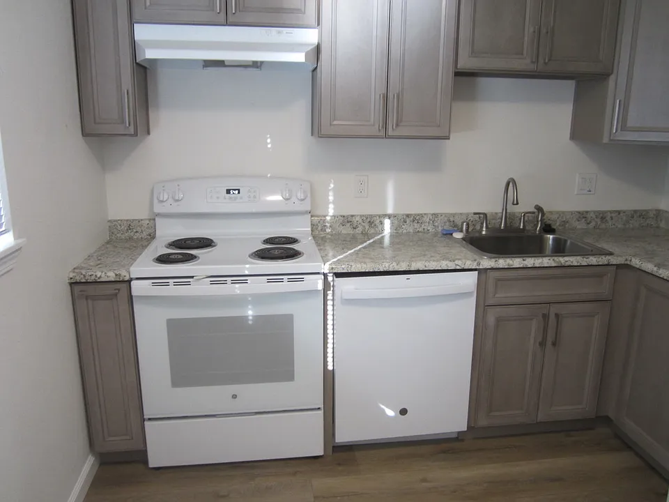 Kitchen with light over electric stove, dishwasher and sink. Bottom cupboard near refrigerator has lazy susan.