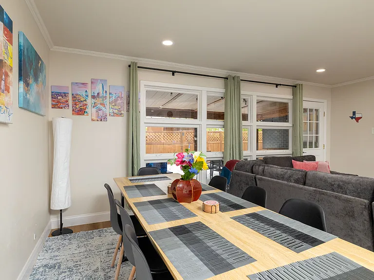 Bright dining area seating 8 with a long table for group meals, modern decor, and large windows overlooking the patio. Flows seamlessly into the cozy living room for easy gathering.