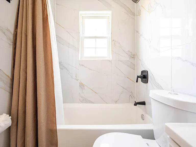 Clean full bath with tub/shower combo, marble-look tile surround, and window for natural light and ventilation.