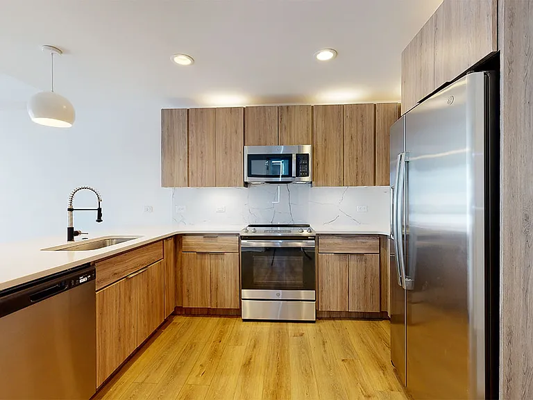 Apartment kitchen with stainless steel appliances, quartz countertops and wood-style flooring.