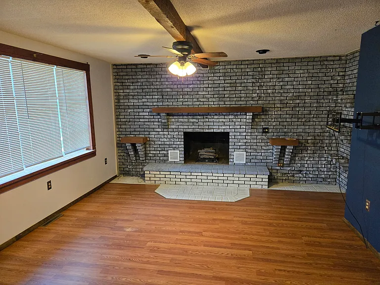 Living room with gas log fireplace (non-vented), exposed beams, ceiling fan and custom painted brick. Bay window overlooks front yard. Laminate wood floors throughout the house.