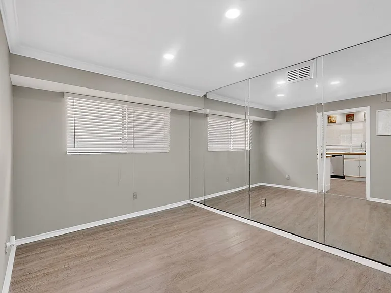 A bright dining area with a wooden floor, window and a mirror wall reflecting the space.
