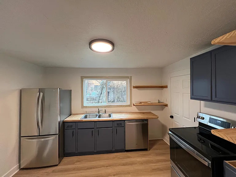 Updated kitchen with stainless steel appliances, butcher block countertops, and open shelving.