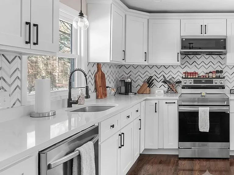 Updated kitchen with ample white cabinetry, generous counters, window over sink, and stainless-steel range and microwave.