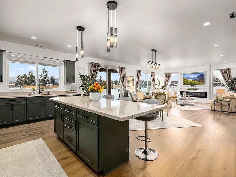 Beautifully designed gathering spaces flow effortlessly together, highlighted by a grand kitchen island, modern lighting, breathtaking mountain views, and a warm fireplace creating the perfect Montana retreat atmosphere.
