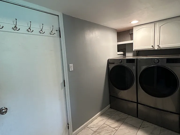 Another view of the laundry room, there is plenty of space for storage below the washer and dryer, and above with the cabinets and shelves. The door that opens to the garage conveniently houses several hooks for coats.
