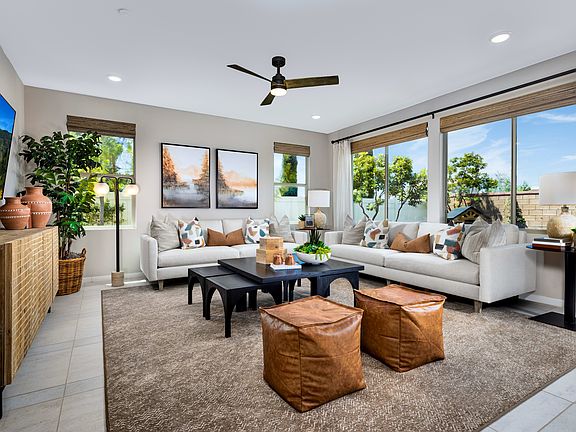 A modern and cozy living room with large windows, a ceiling fan, and various decorative elements suc