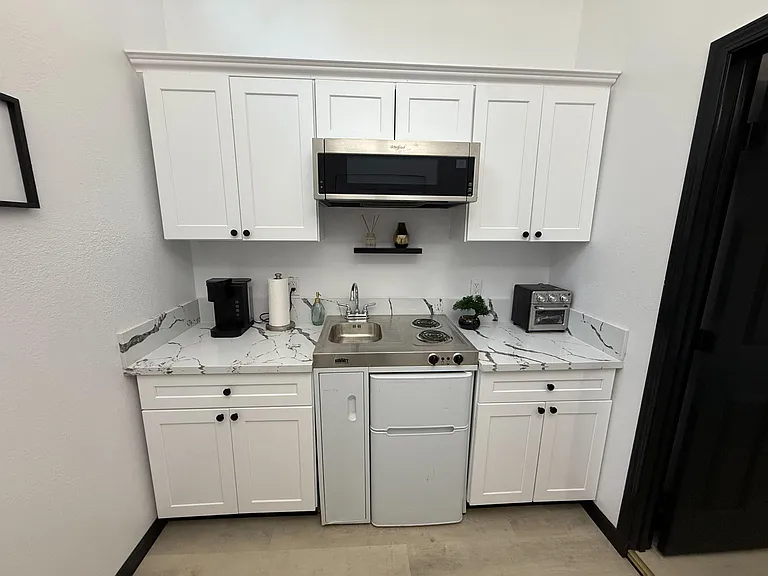 Streamlined kitchenette with shaker cabinetry, marble-look counters, stainless sink, and microwave over a 2-burner cooktop.