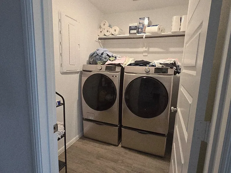 Dedicated laundry room with bright lighting, durable ceramic tile flooring, and built-in shelving for storage, providing a clean and convenient space for everyday laundry needs.