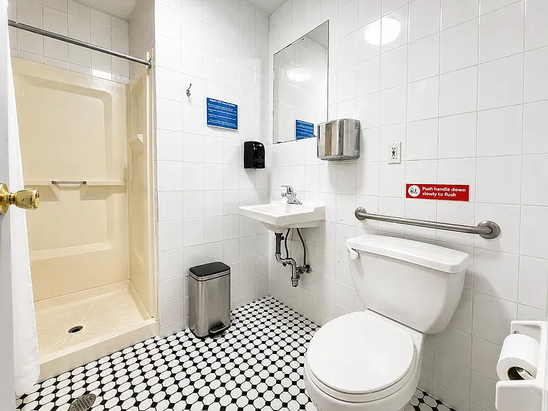 Tiled bathroom with a walk-in shower stall, pedestal sink, wall mirror, and accessible grab bar for added convenience.