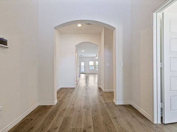 Hallway featuring wood-finish flooring, an arched entryway, recessed lighting, white baseboards, and a modern door with square paneling