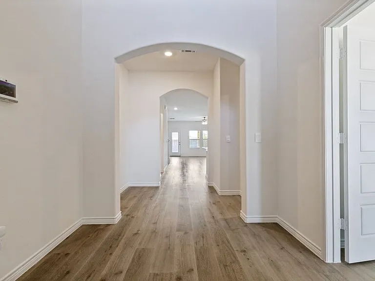 Hallway featuring wood-finish flooring, an arched entryway, recessed lighting, white baseboards, and a modern door with square paneling