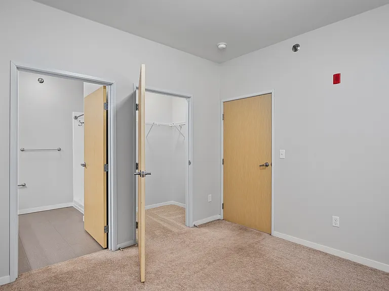 Modern apartment bedroom with plush carpeting, featuring open closet and bathroom access. Modern apartment bedroom with plush carpeting, featuring open closet and bathroom access.