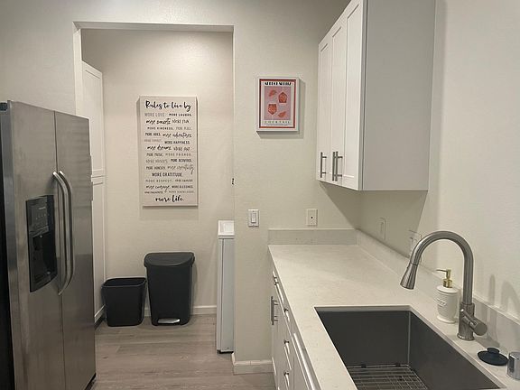 Kitchen sink, white granite counter tops, and an area for laundry are featured with a stacked washer and dryer unit.