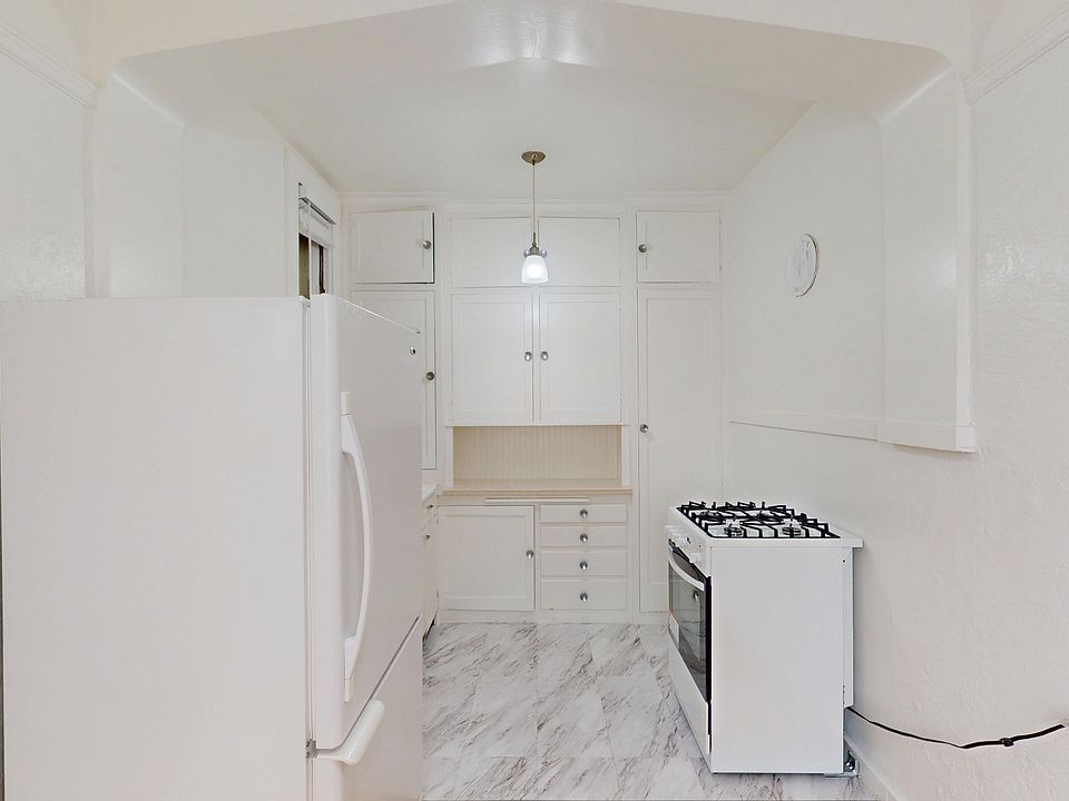Kitchen featuring cabinets, a refrigerator, and a stove, with marble flooring and a pendant light