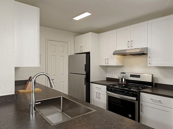 Renovated Package II kitchen with white cabinetry, dark grey laminate countertops, stainless steel appliances, and hard surface flooring