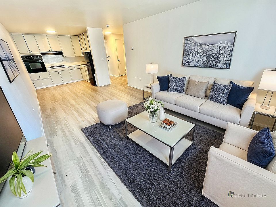 Modern open-concept living room with sleek hardwood floors, plush seating, and elegant decor, leading into a contemporary kitchen with high-end appliances.