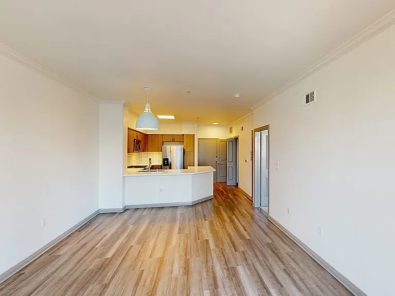 Apartment kitchen with stainless steel appliances, dining and living room with wood-style flooring.