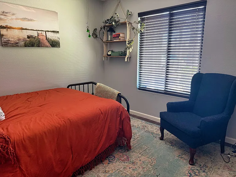 Queen-size bed and armchair with window facing picturesque front yard.