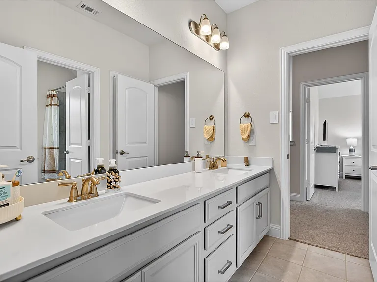 Dual vanity featuring white shaker cabinetry, gold-finish fixtures, and a continuous surface countertop