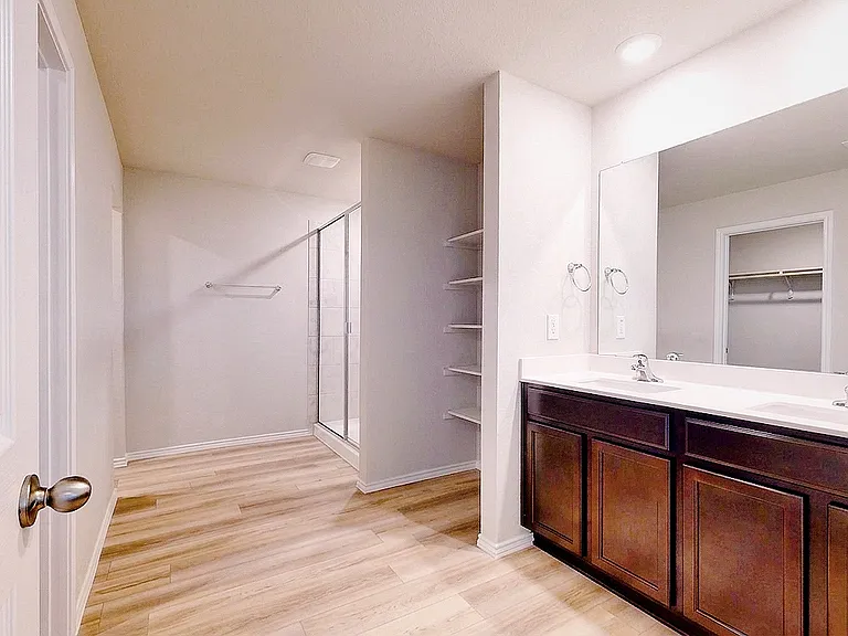 Spacious primary suite bathroom featuring a double-sink vanity, walk-in shower, built-in shelving, and a large walk-in closet _ plenty of storage and room to get ready.