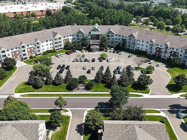 Aerial view of a modern apartment complex with spacious parking, lush greenery, and well-maintained surroundings.